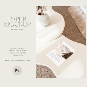 Op de afbeelding: Een witte papiermockup op een witte tafel met een vaas en een tijdschrift. De tekst "PAPER MOCKUP" is in zwart op een witte achtergrond geschreven. De tekst "by Studio Schenk" is in zwart op een witte achtergrond geschreven. De tekst "Purchase includes: 1 A4 Paper mockup PSD file 1 High resolution JPG file 1 Instruction file" is in zwart op een witte achtergrond geschreven. De tekst "The PSD file is optimized to use with: Ps" is in zwart op een witte achtergrond geschreven.
