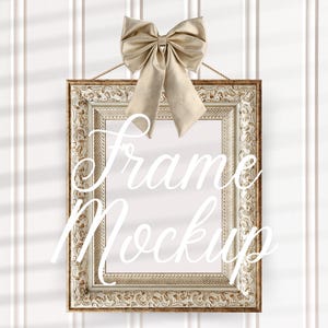 May include: A white ornate picture frame with a gold bow on top. The frame is hanging on a white wall with vertical wood paneling. The text "Frame Mockup" is written in white cursive letters on the frame.