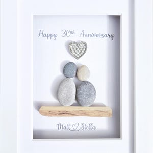 May include: A framed artwork with a white border. The artwork features a heart-shaped embellishment above a grouping of pebbles, with the words "Happy 30th Anniversary" and the names "Matt & Stella" displayed.