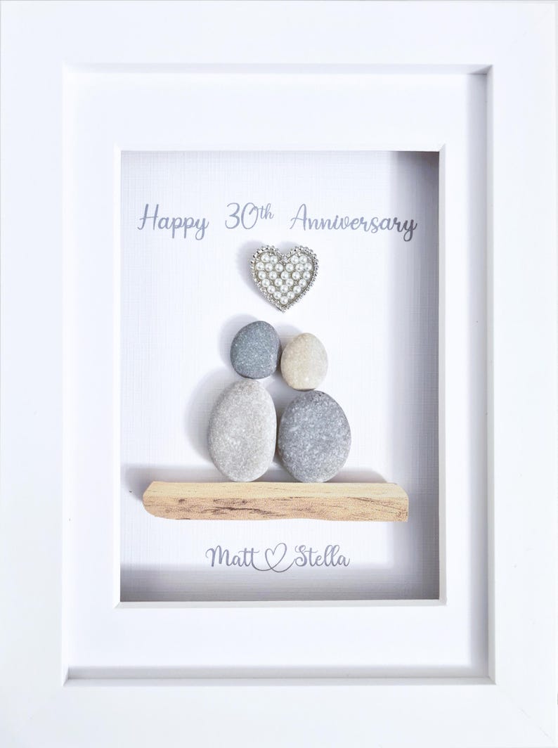 May include: A framed artwork with a white border. The artwork features a heart-shaped embellishment above a grouping of pebbles, with the words "Happy 30th Anniversary" and the names "Matt & Stella" displayed.
