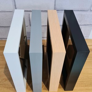 Pode incluir: Quatro molduras de fotos em cores diferentes: branco, cinza, madeira clara e preto. As molduras s&atilde;o todas do mesmo tamanho e formato, e est&atilde;o dispostas em uma fila da esquerda para a direita.