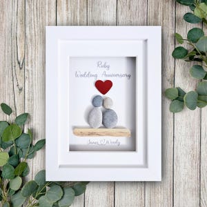 May include: A framed artwork for a Ruby Wedding Anniversary. The white frame surrounds a design with two stone figures, a red heart, and the words "Ruby Wedding Anniversary." The names "James & Wendy" are at the bottom.