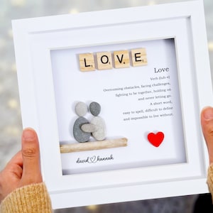 May include: A white frame with a gray stone couple holding hands, a red heart, and the word "LOVE" spelled out with Scrabble tiles. The text below reads "Love Verb (luh- Overcoming obstacles, facing challenges, fighting to be together, holding on and never letting go. A short word, easy to spell, difficult to define and impossible to live without." The bottom of the frame reads "david Channah".