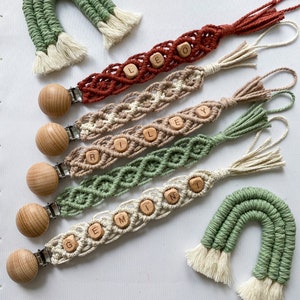 May include: Five crocheted baby teethers with wooden beads spelling out the names Riley, Leo, Gem, Ley, and Min. Two green crocheted rainbows with white fringe.