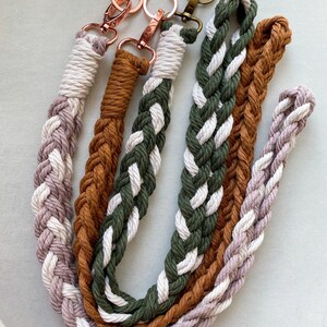 May include: Three braided cotton lanyards featuring rose gold and antique brass swivel clasps. The lanyards are crafted from twisted cord in color combinations of mauve and white, solid rust brown, and olive green mixed with white.