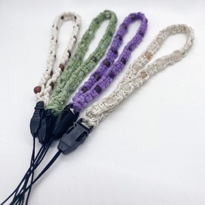 May include: Four crocheted phone straps with different colored beads and black clasps. The straps are made with white, green, purple, and brown yarn.