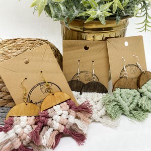 May include: Three pairs of handmade wooden earrings with macrame fringe. The earrings are displayed on brown card stock with the words "Northern" and "Tattered" printed on them. The fringe is in shades of pink, white, and green.