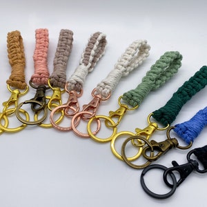 May include: A set of ten colorful macrame keychains with gold, silver, and bronze key rings. The keychains are made with different colored cords and are tied in a variety of knots.