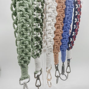 May include: A set of six colorful macrame keychains with silver and gold clasps. The keychains are made with different colored cords and have a variety of knot patterns.