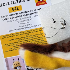 May include: A needle felting kit to create a bee. The kit includes yellow, brown, and white wool roving, felting needles, a foam pad, plastic eyes, and a key chain. The instructions are printed on a white card with the title "Bee" in yellow letters.