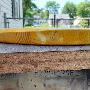 Pu&ograve; includere: Un tagliere rotondo in legno, di colore giallo chiaro. &Egrave; realizzato con pi&ugrave; pezzi di legno, che mostrano il motivo della venatura. Il tagliere &egrave; appoggiato su una superficie a motivi. Diametro: circa 30 cm.