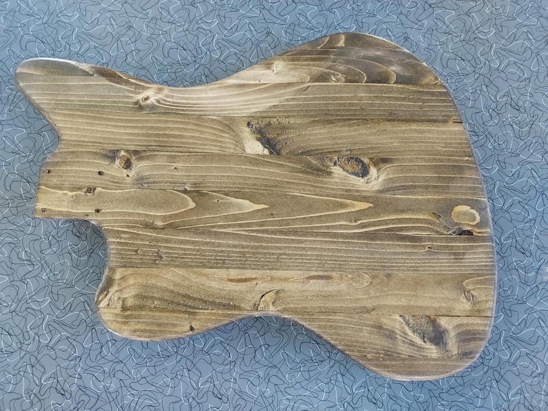 Op de afbeelding: Een gitaarvormige houten snijplank met een natuurlijke houtnerf afwerking. De plank heeft een glad oppervlak en afgeronde randen, met een lichtbruine kleur. De houtnerf is zichtbaar.