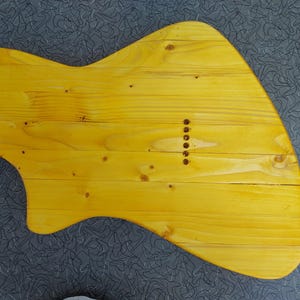 Pu&ograve; includere: Un corpo di chitarra in legno giallo, realizzato con assi di legno. Il corpo ha una forma unica con un fondo curvo e un corno superiore appuntito. Sei fori sono forati per le corde.