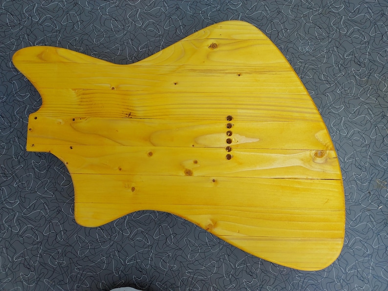 Pu&ograve; includere: Un corpo di chitarra in legno giallo, realizzato con assi di legno. Il corpo ha una forma unica con un fondo curvo e un corno superiore appuntito. Sei fori sono forati per le corde.