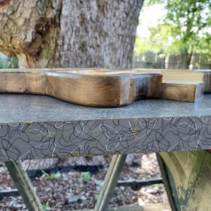 Puede incluir: Una tabla de madera gruesa y sin terminar con un borde oscuro, te&ntilde;ido y texturizado. La pieza de madera presenta un patr&oacute;n de grano natural y una superficie superior lisa y clara, mostrando el material crudo y la artesan&iacute;a del objeto.