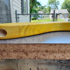 Pu&ograve; includere: Un corpo di chitarra in legno massello, non rifinito, di colore giallo. Il corpo ha una forma arrotondata e un foro per un componente. &Egrave; appoggiato su una superficie a fantasia. La venatura del legno &egrave; visibile.