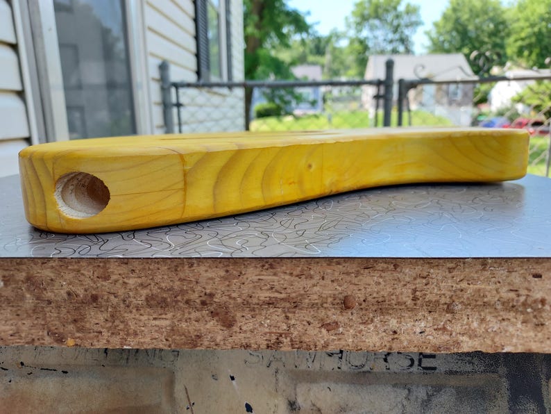 Pu&ograve; includere: Un corpo di chitarra in legno massello, non rifinito, di colore giallo. Il corpo ha una forma arrotondata e un foro per un componente. &Egrave; appoggiato su una superficie a fantasia. La venatura del legno &egrave; visibile.