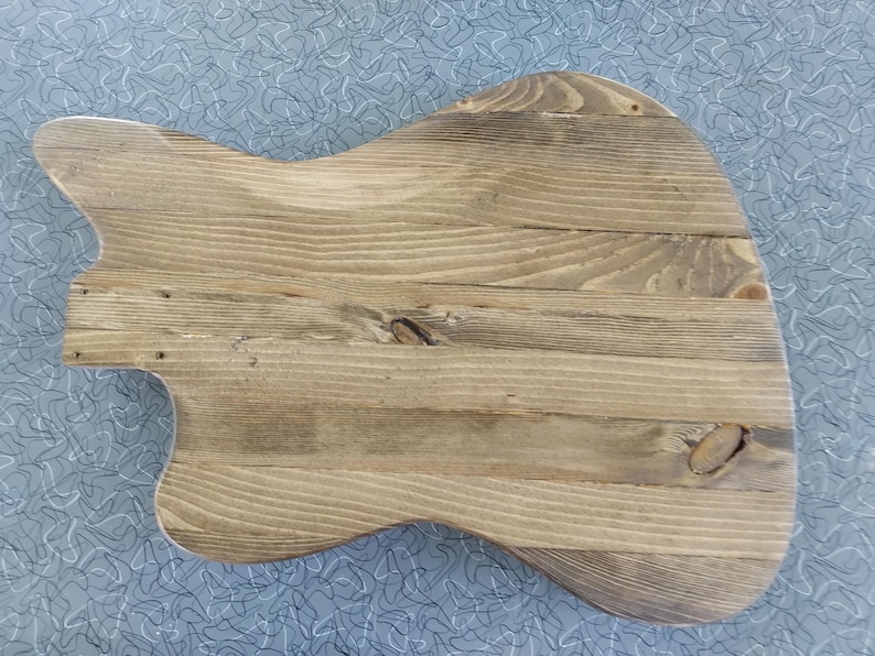 Puede incluir: Un cuerpo de guitarra en bruto construido con varias tablas horizontales de madera marr&oacute;n claro con vetas y nudos visibles. La pieza presenta una forma asim&eacute;trica contorneada con un recorte en el lado izquierdo y una superficie lisa sin acabado.