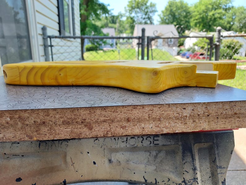 Pu&ograve; includere: Un corpo di chitarra incompiuto in legno giallo chiaro. Il corpo &egrave; stato levigato e poggia su una superficie a motivi. Il corpo della chitarra &egrave; in fase di costruzione. Il corpo della chitarra &egrave; lungo circa 76 cm.