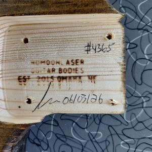 Puede incluir: Un bolsillo de m&aacute;stil de cuerpo de guitarra de madera clara con cuatro orificios pretaladrados. La madera est&aacute; marcada con el texto #4365, NUMOON LASER GUITAR BODIES, EST 2015 OMAHA NE, y una fecha escrita a mano 06/03/26 con una firma.