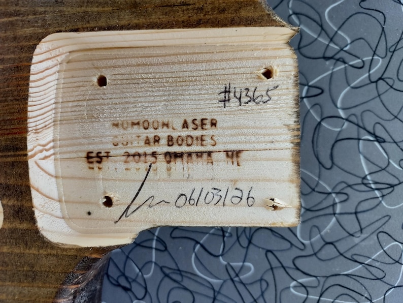 Puede incluir: Un bolsillo de m&aacute;stil de cuerpo de guitarra de madera clara con cuatro orificios pretaladrados. La madera est&aacute; marcada con el texto #4365, NUMOON LASER GUITAR BODIES, EST 2015 OMAHA NE, y una fecha escrita a mano 06/03/26 con una firma.