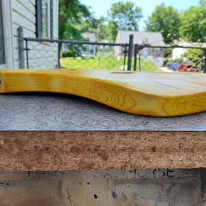 Pu&ograve; includere: Un corpo di chitarra in legno massello, tinto di giallo, che mostra le venature naturali del legno. Il corpo ha un design curvo ed ergonomico, con una superficie liscia e rifinita. Il corpo della chitarra &egrave; appoggiato su una superficie a motivi.