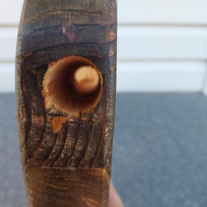 May include: Close-up of a section of dark brown wood with a drilled hole. The hole is cylindrical and appears to be freshly drilled. The wood grain is visible, and the edges of the hole show some splintering.