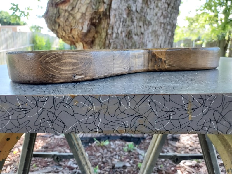 Puede incluir: Un cuerpo de guitarra el&eacute;ctrica de madera maciza con un acabado te&ntilde;ido en marr&oacute;n oscuro, que muestra un patr&oacute;n de veta de madera natural prominente. La pieza presenta un borde liso y contorneado con una superficie superior plana.