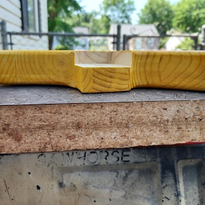 Pu&ograve; includere: Un vassoio in legno fatto a mano con finitura a venature naturali. Il vassoio ha una forma rettangolare con una sezione ritagliata. Il legno ha una calda tonalit&agrave; giallo dorato. Il vassoio &egrave; probabilmente per servire o esporre.