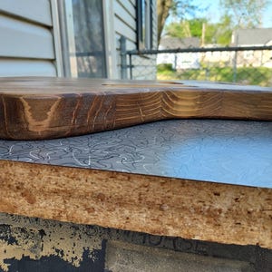 May include: A handcrafted, wooden guitar body with a natural, stained finish. The body is shaped with smooth curves and a hole for the neck. The wood grain is visible, showcasing the natural texture and color variations. The guitar body is resting on a patterned surface.