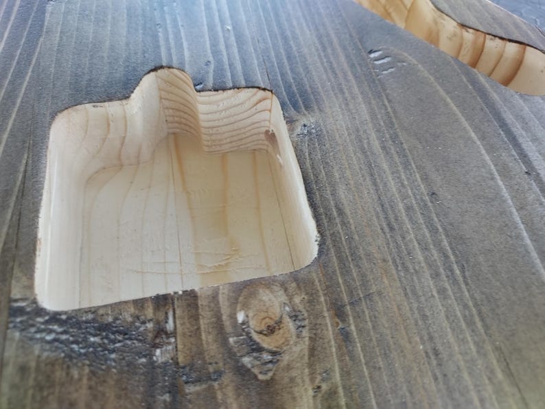 Op de afbeelding: Close-up van een houten oppervlak met een uitgesneden gedeelte. Het hout is grijs gebeitst en het uitgesneden gedeelte is van natuurlijk hout. Het ontwerp suggereert een handvat of een verzonken kenmerk.