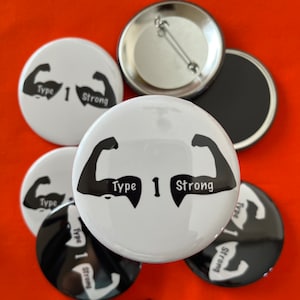 May include: Six white and black button badges with the text "Type 1 Strong" and a graphic of two bicep muscles. The buttons are arranged in a circle on a red surface.