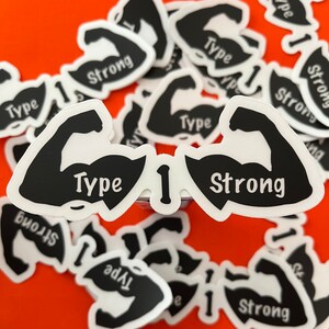 May include: A close-up of a sticker with a black silhouette of two bicep muscles, one with the word "Type" and the other with the word "Strong". The sticker is on a red background and there are other stickers in the background.