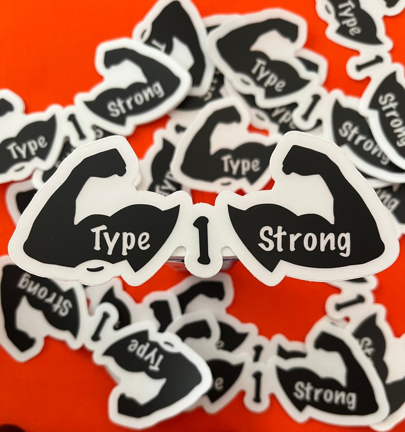 May include: A close-up of a sticker with a black silhouette of two bicep muscles, one with the word "Type" and the other with the word "Strong". The sticker is on a red background and there are other stickers in the background.