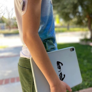May include: A young person wearing a blue and white tank top with a medical device on their arm, holding a white tablet with a black sticker that says "Type 1 Strong".