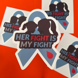 May include: A blue ribbon with a red blood drop, and two silhouettes of people facing each other. The text "HER FIGHT IS MY FIGHT" is written in bold, white letters on the ribbon.