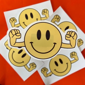 May include: Five yellow smiley face stickers with arms raised in a flexing pose. The stickers are on white paper.