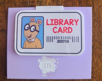 Puede incluir: Una tarjeta de biblioteca blanca con un personaje de dibujos animados que lleva gafas y una camisa amarilla. La tarjeta dice "LIBRARY CARD" en letras rojas y tiene un código de barras con el número 2101708.