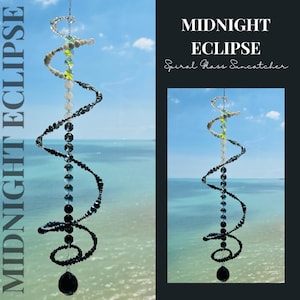 以下が含まれることがあります： 「Midnight Eclipse」と題された螺旋状のガラス製サンキャッチャー。上部の透明・白色から下部の濃紺・黒色へと変化するグラデーションのビーズが細い金属ワイヤーに連なり、一番下には大きな黒いクリスタルのドロップが付いています。