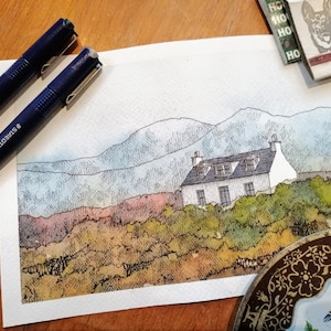 May include: A watercolor painting of a white cottage with a black roof, surrounded by green bushes and trees. The cottage is set against a backdrop of blue and green mountains.