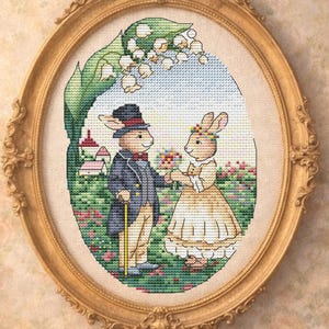 Könnte beinhalten: Ein gerahmtes Kreuzstich-Kunstwerk mit zwei anthropomorphen Kaninchen in formeller Kleidung. Das männliche Kaninchen trägt einen Zylinder und hält einen Stock, während das weibliche Kaninchen ein Kleid trägt. Das Kunstwerk ist in einer Gartenszene in einem ovalen Goldrahmen.