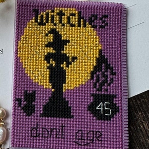 Könnte beinhalten: Eine weiße Karte mit dem Text "Dear My Beautiful Witch. Witches don't age. Happy birthday dear!", ein Perlenarmband mit goldfarbenen Zwischenelementen und ein violetter Kreuzstich-Aufnäher mit einer Hexe, einem gelben Mond, einer Katze und der Zahl 45.