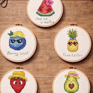 Op de afbeelding: Vijf borduurringen met fruitontwerpen. De ontwerpen omvatten een watermeloen, een bosbes, een ananas, een aardbei en een avocado, elk met een hoed. Tekst omvat "One in a melon", "Berry cool", "Pine-tastic", "Berry sweet" en "Avoc-adorable".