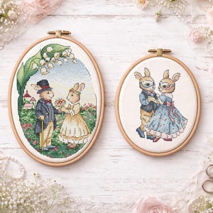 Könnte beinhalten: Zwei ovale Stickrahmen mit Hasenpaaren. Einer zeigt Hasen in formeller Kleidung, der andere mit Masken. Die Rahmen befinden sich auf einem weißen Holzgrund mit floralen und Spitzenakzenten.