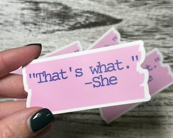 May include: Pink sticker with a white border and a torn edge. The sticker has the text "That's what." -She in blue text.