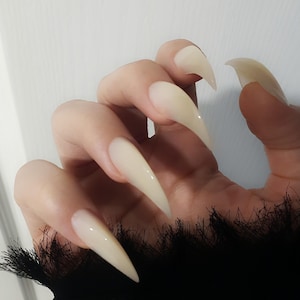 May include: Close-up of a hand with long, pointed, white acrylic nails.
