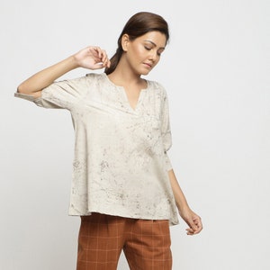 May include: A woman is wearing a white, loose-fitting top with a V-neck and brown checkered pants.