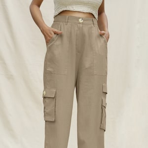 Puede incluir: Pantalón cargo beige con múltiples bolsillos y cierre de botón. El pantalón está hecho de una tela ligera y tiene un corte holgado.