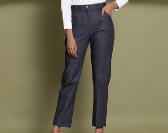 Puede incluir: Un pantalón vaquero azul oscuro de pierna recta. El pantalón tiene cierre de botón y cremallera y trabillas para el cinturón. La modelo lleva una camisa blanca de botones y tacones rosas.