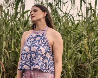 May include: A woman wearing a blue and pink floral halter top with a pink and white striped skirt. She is standing in a field of tall green grass.